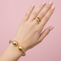 Gold twisted rope bangle and ring set worn on hand with pink background