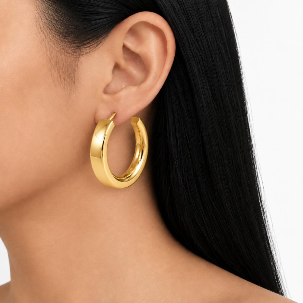 Wide flat gold hoop earring worn on an ear with black hair against a white background