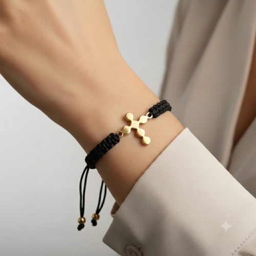 Gold budded cross bracelet worn on wrist with black macramé cord