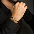 Black enamel cross bracelet gold plated on black macramé cord worn on man's wrist
