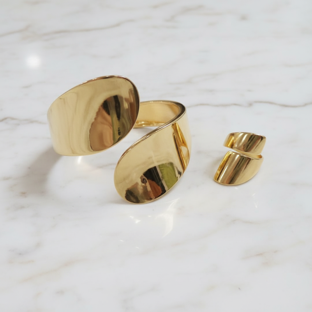 Gold sculptural cuff bracelet and ring set on marble background