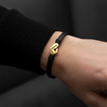 Black leather bracelet with gold mother and child charm worn on man's wrist